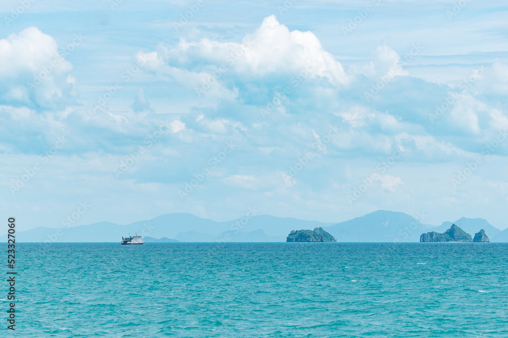 View of the turquoise sea and islands on a sunny summer day.  A ship sails in the distance.  Mountain silhouettes in the background.