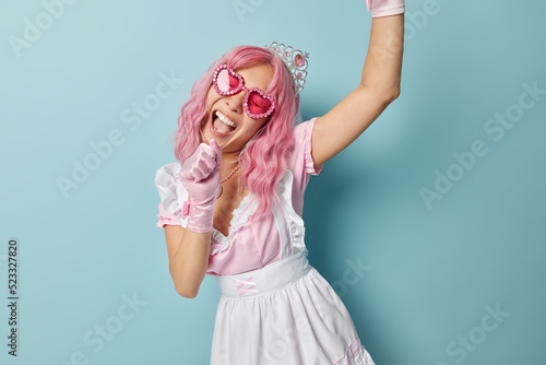 Foto Cheerful upbeat woman with pink hair pretends being princess keeps arm near open