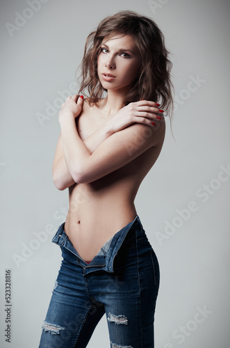 Studio portrait of sexy young girl. Pretty woman dressed in jeans. Seductive sweet lady, topless (nipples closed)