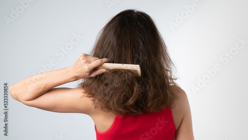A woman tries to comb her tangled hair from behind with a comb - hair problems