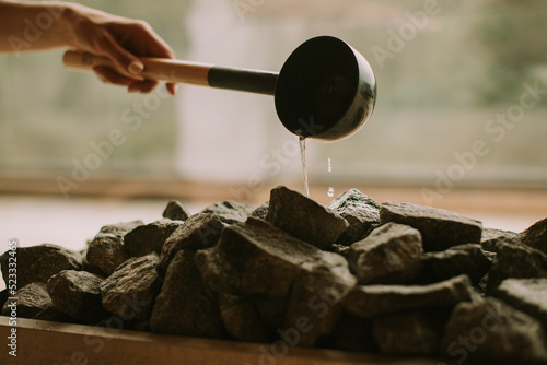 Hand of young woman pouring water on hot rocks in the sauna photo