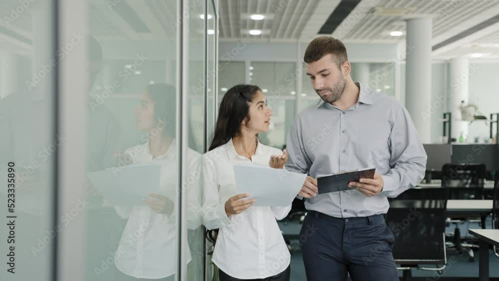 Business young man and woman colleagues stand in office communicate discuss joint project girl trainee asks clarifies details task talks with mentor at workplace creates ideas professional teamwork Business young man and woman colleagues stand in office communicate discuss joint project girl trainee asks clarifies details task talks with mentor at workplace creates ideas professional teamwork