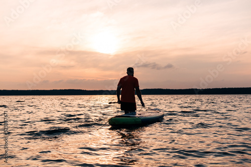 Joyful red bearded man in sunglasses is training on a SUP board on a large lake during sunny day. Stand up paddle boarding - awesome active recreation in nature.  © MarijaBazarova
