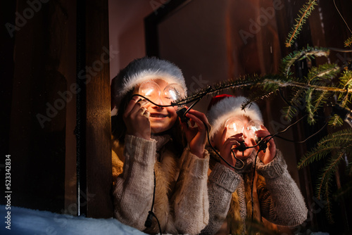 Two cheerful children are playing with a retro garland with light bulbs. Happy family celebrating Christmas and New Year. Children decorate the Christmas tree.