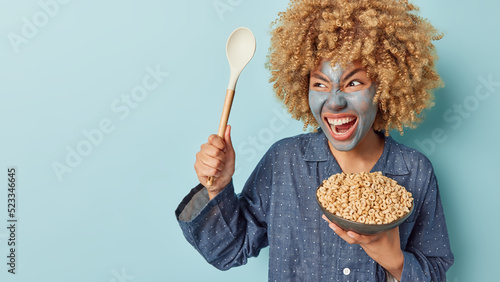 Photo Angry curly haired woman yells with annoynace at loud neighbours holds bowl of c