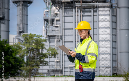 Engineer wearing uniform ,helmet and glass stand hand holding detail file document, inspection and surveying work site progress with oil refinery power industrial factory background