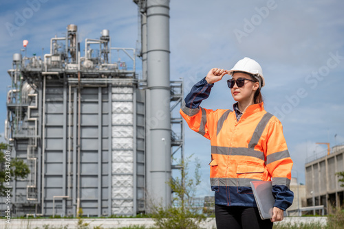 Engineer wearing uniform ,helmet and glass stand hand holding detail file document, inspection and surveying work site progress with oil refinery power industrial factory background