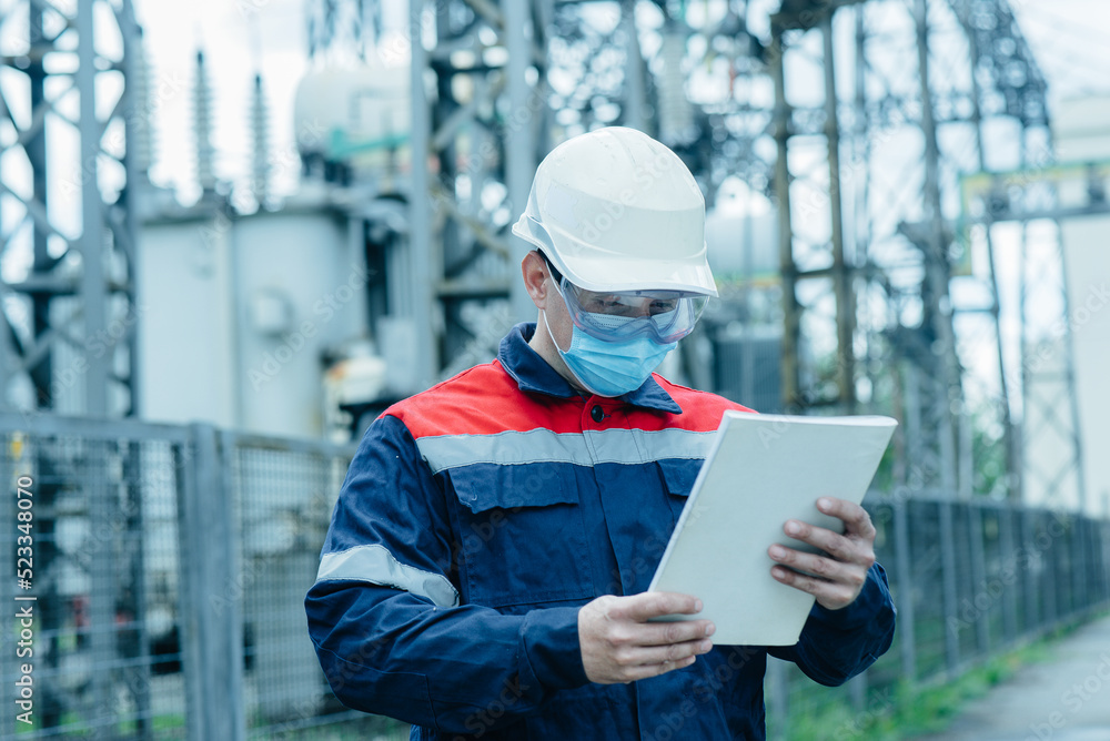 A masked power engineer during a pandemic inspects the modern equipment of an electrical substation before commissioning. Energy and industry. Scheduled repair of electrical equipment. A masked power engineer during a pandemic inspects the modern equipment of an electrical substation before commissioning. Energy and industry. Scheduled repair of electrical equipment.