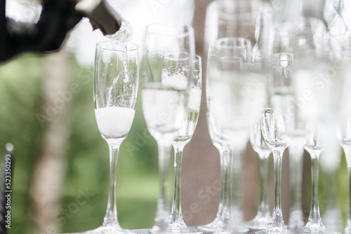 Bartender pouring champagne or wine into wine glasses on the table at the outdoors solemn wedding ceremony. 