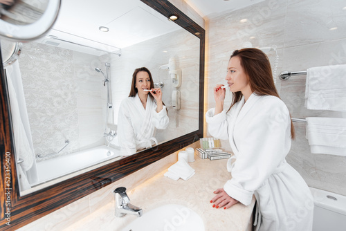 A young beautiful girl is brushing her teeth in a beautiful white bathroom. A fresh good morning at the hotel. Rest and travel. Hotel recreation, and tourism.