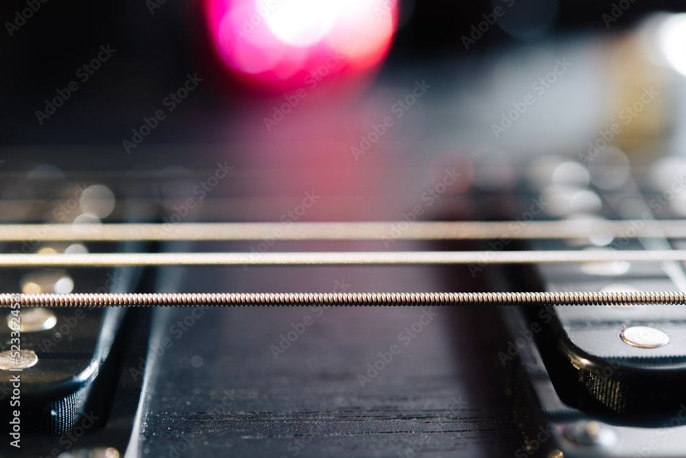 Details of the body and fretboard of an electric guitar. Stage lighting, light music.	