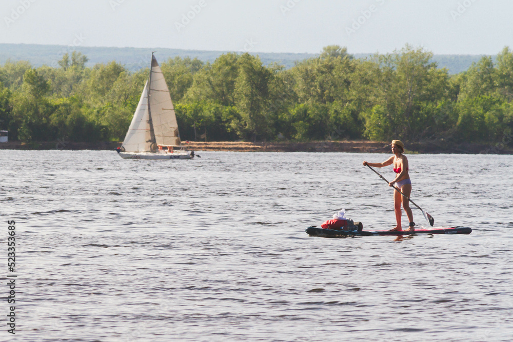 Naklejka premium Men, friends ride SUP boards on a big river during sunrise.