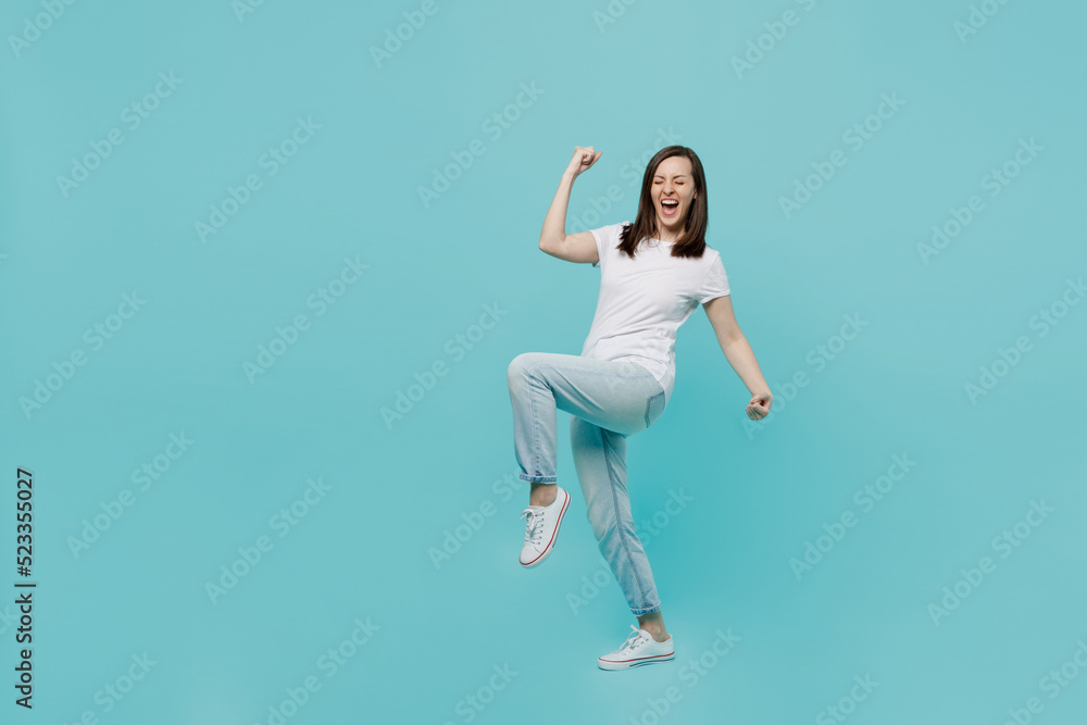 Full body side view young woman 20s she wear white t-shirt doing winner gesture celebrate clenching fists say yes isolated on plain pastel light blue cyan background studio. People lifestyle concept.