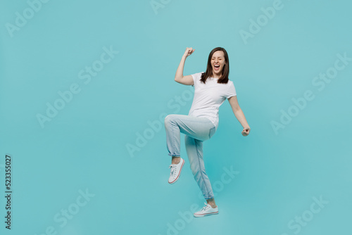 Full body side view young woman 20s she wear white t-shirt doing winner gesture celebrate clenching fists say yes isolated on plain pastel light blue cyan background studio. People lifestyle concept.