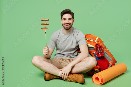 Full body young traveler white man near backpack stuff mat sit roasted sausages on stick isolated on plain green background Tourist lead active healthy lifestyle Hiking trek rest travel trip concept. #523355894
