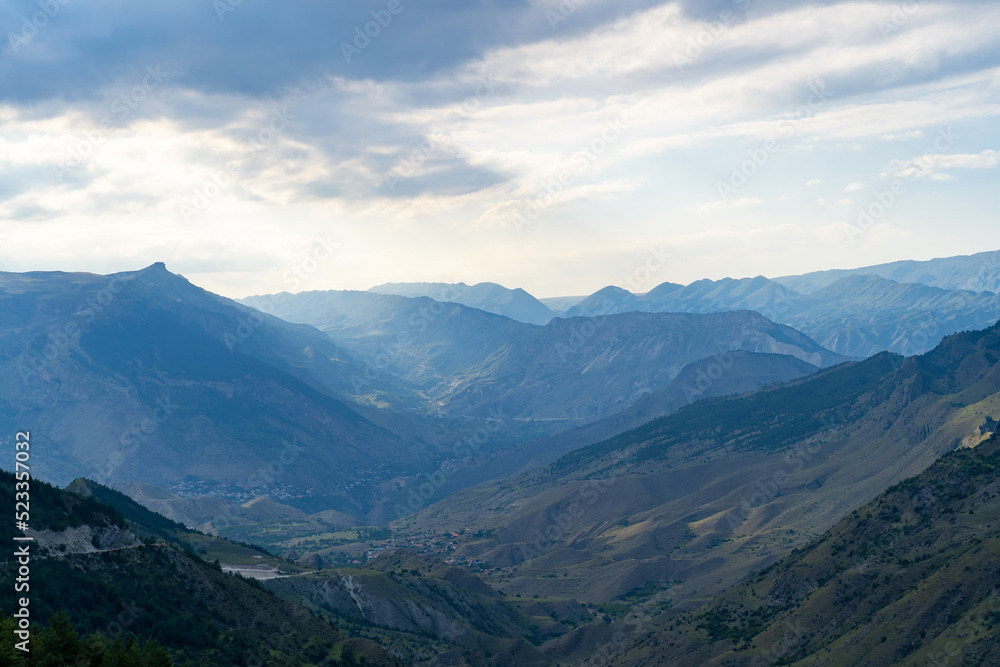 Amazing landscape of mountain range with sunset sky and clouds and rural village in mountain valley in Dagestan. Scenery of mountain layer at dusk. Amazing landscape of mountain range with sunset sky and clouds and rural village in mountain valley in Dagestan. Scenery of mountain layer at dusk.
