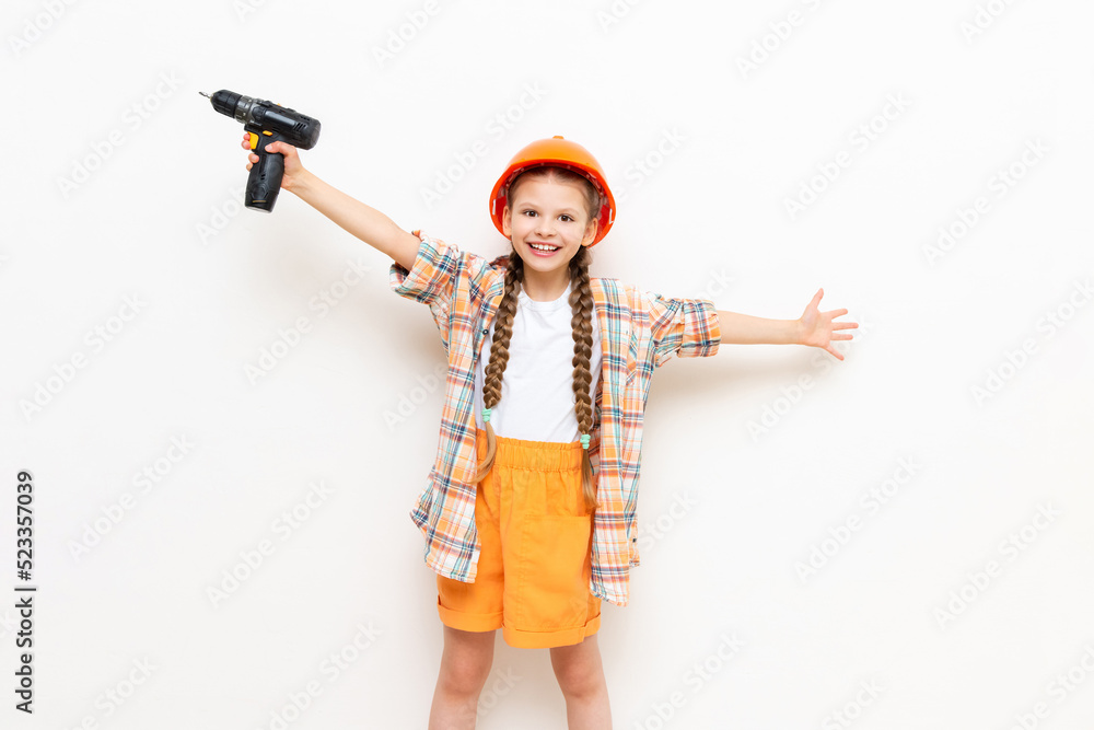 A child in a construction helmet and with a drill in his hands on a white isolated background. A little girl with pigtails is preparing for repair by spreading her arms in different directions. A child in a construction helmet and with a drill in his hands on a white isolated background. A little girl with pigtails is preparing for repair by spreading her arms in different directions.