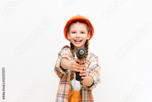 A little girl with a drill and wearing a protective construction helmet depicts a builder on a white isolated background. The concept of repair.