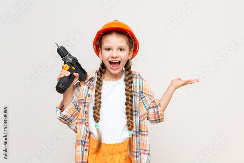 A little girl with a drill in her hand holds your advertisement on a white isolated background in the palm of her hand. The concept of renovation in the children's room. © Юлия Дьякова