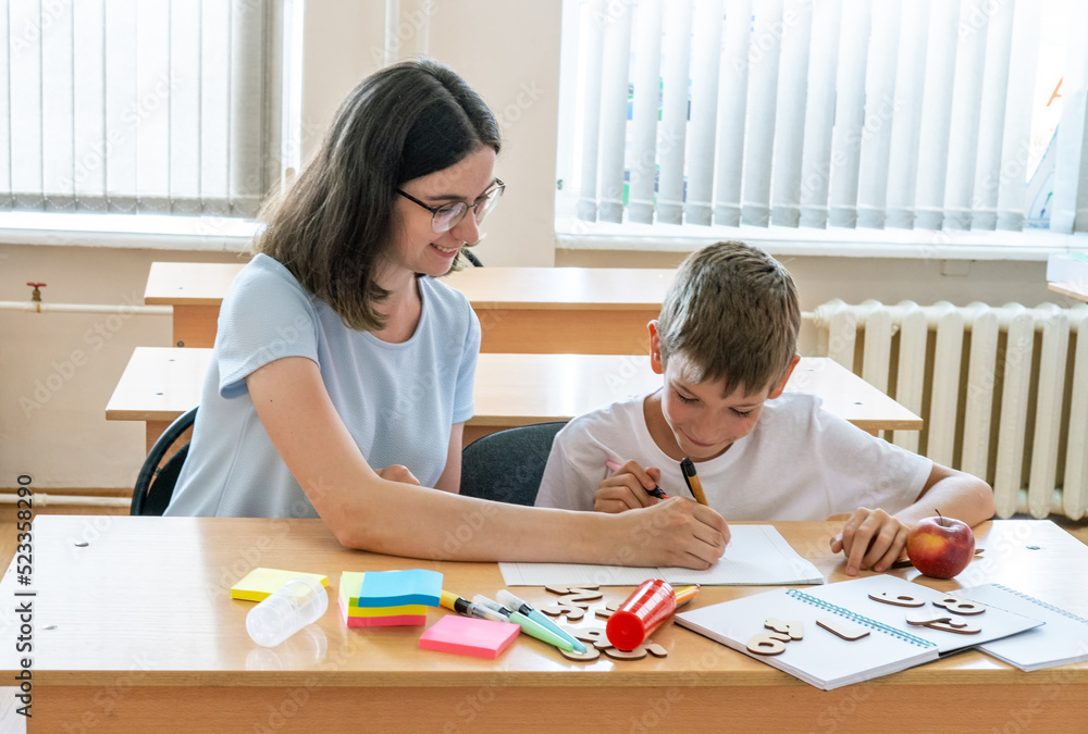 A boy and a teacher doing homework, writing text in a notebook at the table. A mother helps her son write in a notebook A boy and a teacher doing homework, writing text in a notebook at the table. A mother helps her son write in a notebook