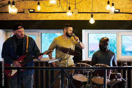 Fotografie Portrait of three young intercultural men in casualwear singing in microphone an