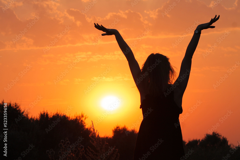 Silhouette of a woman with her hands raised up against the backdrop of a beautiful sunset. Silhouette of a woman with her hands raised up against the backdrop of a beautiful sunset.