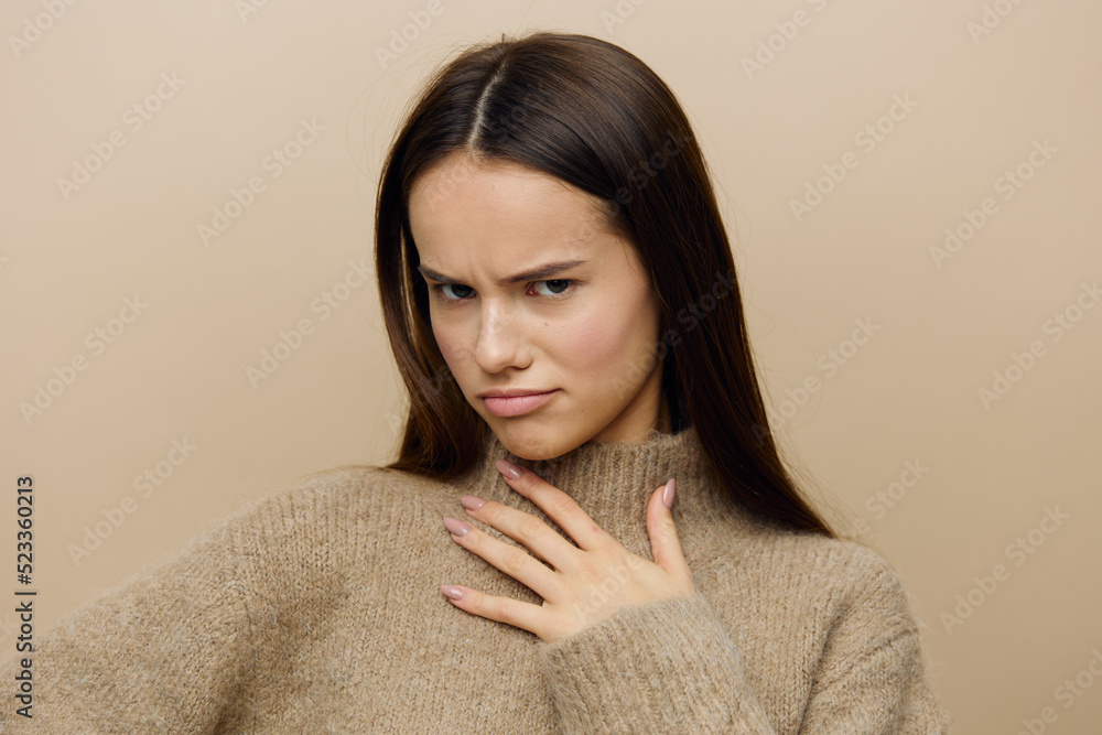 an emotional, vividly expressing her emotions woman stands on a beige background and holding her hand on her chest looks at the camera. Horizontal Studio Photography an emotional, vividly expressing her emotions woman stands on a beige background and holding her hand on her chest looks at the camera. Horizontal Studio Photography