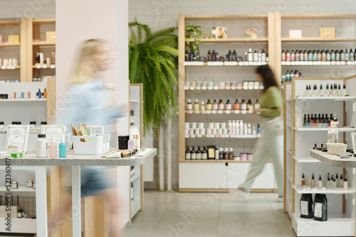 Blurry motion of two young women moving along displays with self care items such as bodycare, skincare, nailcare and makeup products photo