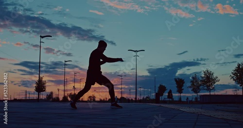 professional fighter is training in evening in city park, dark silhouette against sunset, 4K, Prores