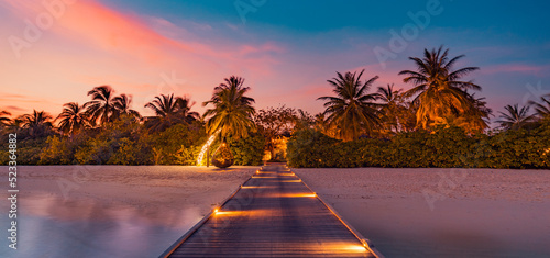 Amazing sunset panorama at Maldives. Luxury resort pier pathway, soft led lights into paradise island. Beautiful evening sky and colorful clouds. Romantic beach background for honeymoon vacation photo
