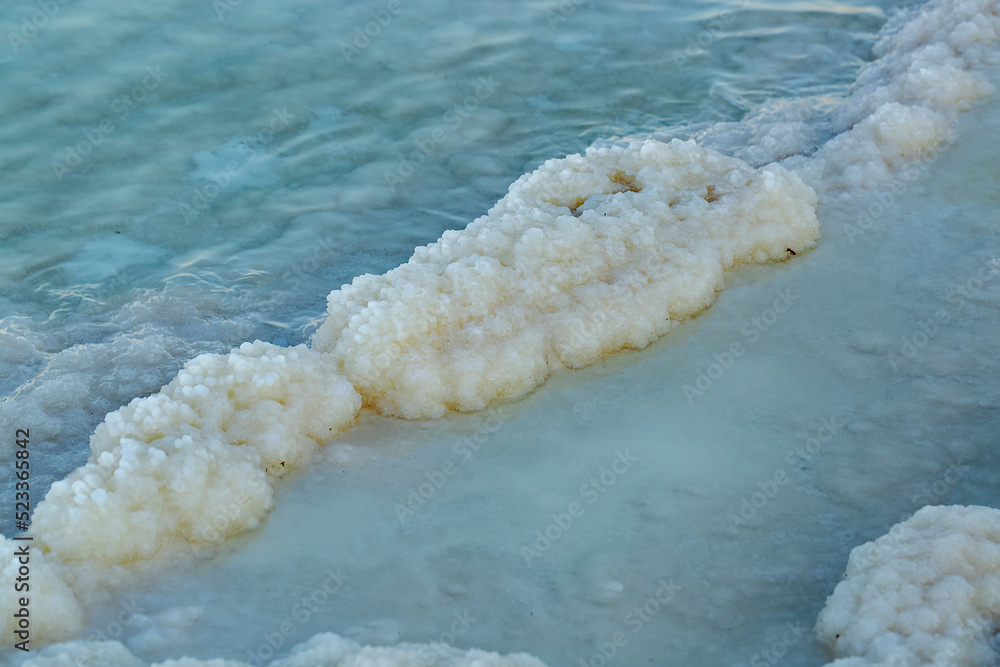 Fototapeta premium Natural sea-salt beach, seashore background. Texture of Dead sea coastline. Salt crystals at sunset, close up. Salty sea shore. Organic salt crystal on the Dead Sea shore. Travel Photos of Israel.