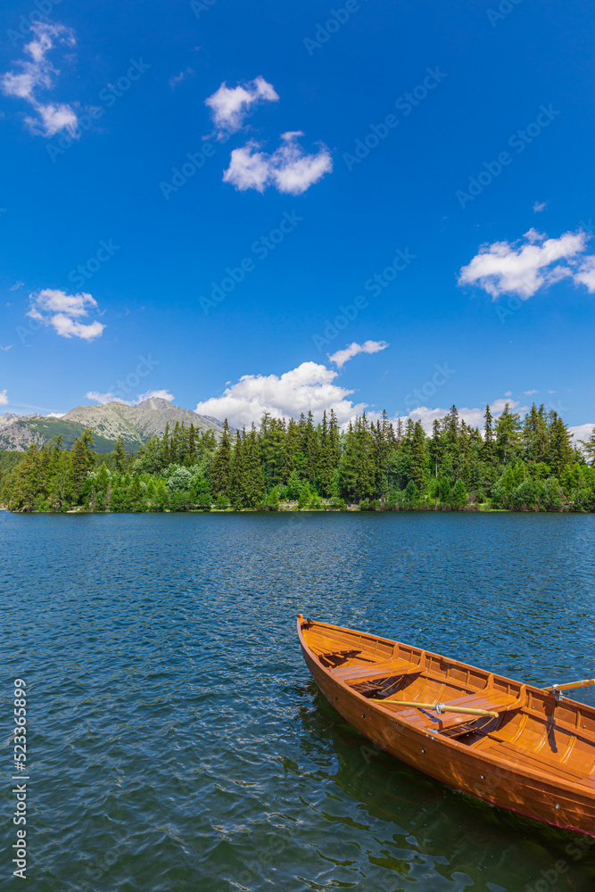 Mountain lake with coniferous forest, wooden boat sunny blue sky, idyllic freedom travel background. Romantic tourist place. National Park High Tatras, Europe. Beautiful nature landscape idyllic view Mountain lake with coniferous forest, wooden boat sunny blue sky, idyllic freedom travel background. Romantic tourist place. National Park High Tatras, Europe. Beautiful nature landscape idyllic view