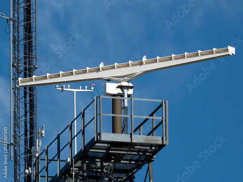 A rotating antenna in white on a blue sky background in bright daylight