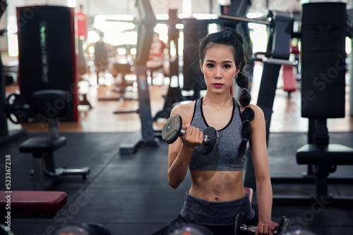 Young fitness woman doing biceps exercises while sitting on the bench and raising dumbell in the gym. Fitness concept of healthy lifestyle. Fitness woman in the gym.