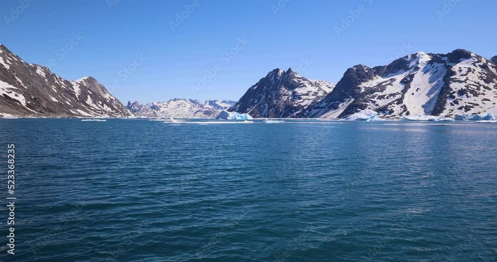 Melting icebergs by the coast of Greenland, on a beautiful summer day - General view of iceberg and moutains from a moving boat - Greenland Melting icebergs by the coast of Greenland, on a beautiful summer day - General view of iceberg and moutains from a moving boat - Greenland