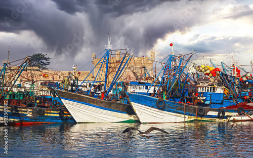 Wallpaper Mural Storm clouds over north african fishing harbour, traditional old moroccan boats, port fortress - Essaouira, Morocco (focus on left white ship bow) Torontodigital.ca