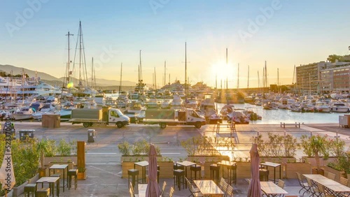 Beautiful sunrise over the harbor in Monaco timelapse. Luxury yachts are illuminated in the morning light. Colorful sky at summer day. Tables and chairs on foreground photo