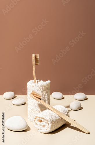 Organic wooden bamboo toothbrushes, towels and white sea pebbles on terracotta and beige background. Natural beauty and health concept. Eco-friendly zero waste design with copy space.