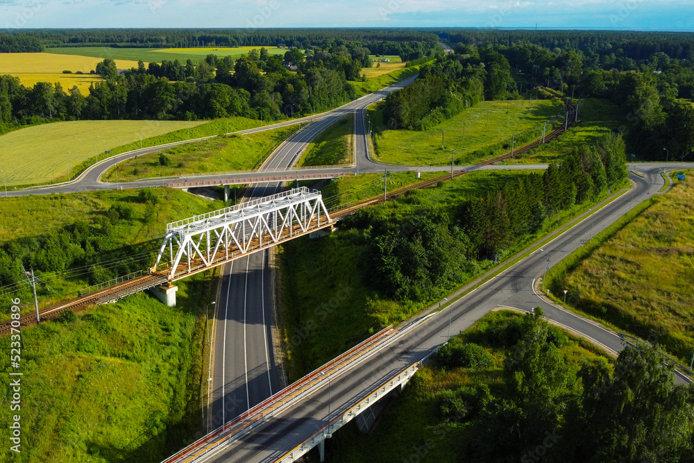 Aerial view of an automobile road junction intersection with bridges and trucks and cars on a sunny day against a green lawn Aerial view of an automobile road junction intersection with bridges and trucks and cars on a sunny day against a green lawn