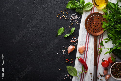 Frying pan white , black empty plate, basil leaves and spices on dark stone background. Abstract food background. Top view of dark rustic kitchen table with wooden cooking utensils, frame. Mock up.
