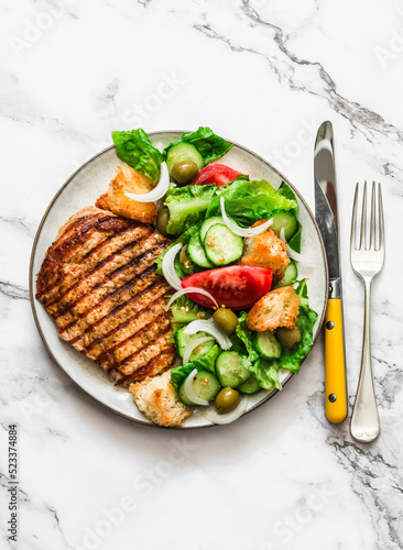 Grilled pork chop and Italian panzanella salad on a light marble background, top view