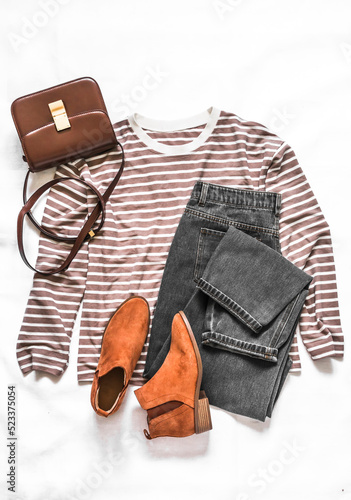 Women's clothing set - long sleeve striped pullover, crossbody bag, gray jeans, suede chelsea boots on a light background, top view