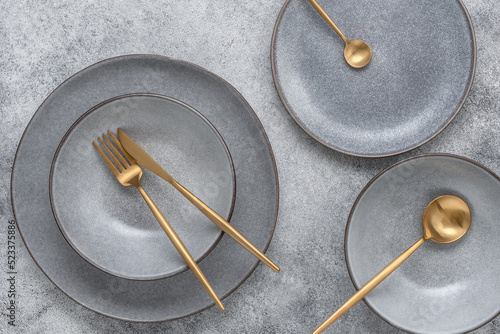 Gray plates and golden cutlery, gray grunge background. Dishes for table setting. Modern craft ceramics. Top view, flat lay.