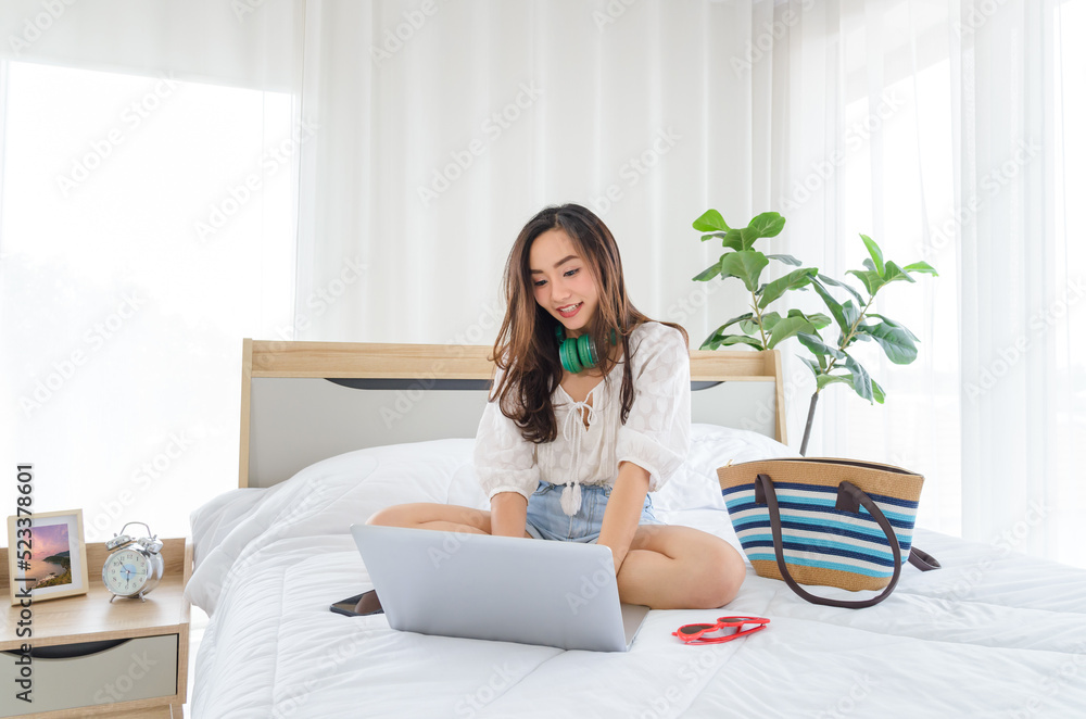 Asian girl student sit on bed with green headphone watch video online webinar learn on laptop. e-learning course video conference pc call in bedroom at home. Social distancing self isolation.