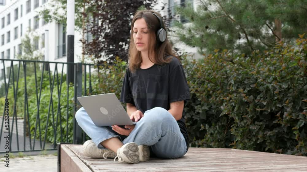 Young woman is engaged outdoors in the park using a laptop on a summer day. A female freelancer working at a distance of online distances. Young woman is engaged outdoors in the park using a laptop on a summer day. A female freelancer working at a distance of online distances.