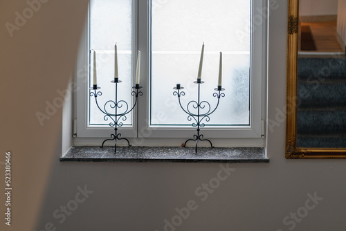 Five candles in two candlesticks on a marble window sill on a cloudy morning, in a large mirror on the wall in a gold frame the stairs are reflected, the interior of a private hotel in Austria photo