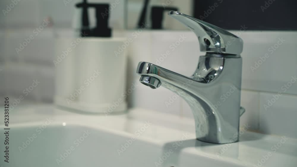 Static video of a faucet in a bathroom with dripping water. Faucet malfunction, drops of clean water dripping into the white washbasin