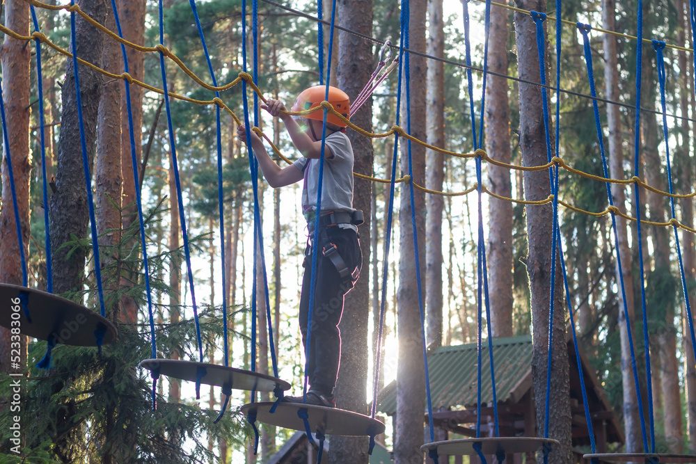 A boy overcomes obstacles in a rope park, a child with insurance and a protective helmet holds on to the ropes and passes over the abyss A boy overcomes obstacles in a rope park, a child with insurance and a protective helmet holds on to the ropes and passes over the abyss