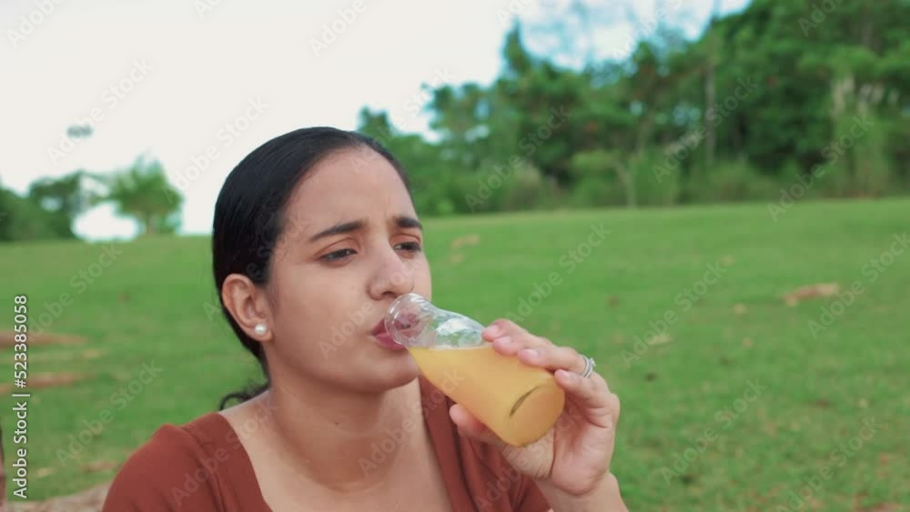 latin woman drinking orange juice, seated in the field, close-up latin woman drinking orange juice, seated in the field, close-up