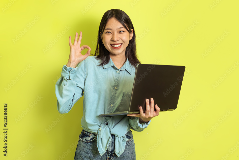 Asian Lady Holding Laptop Computer Gesturing Okay On Yellow Background Asian Lady Holding Laptop Computer Gesturing Okay On Yellow Background